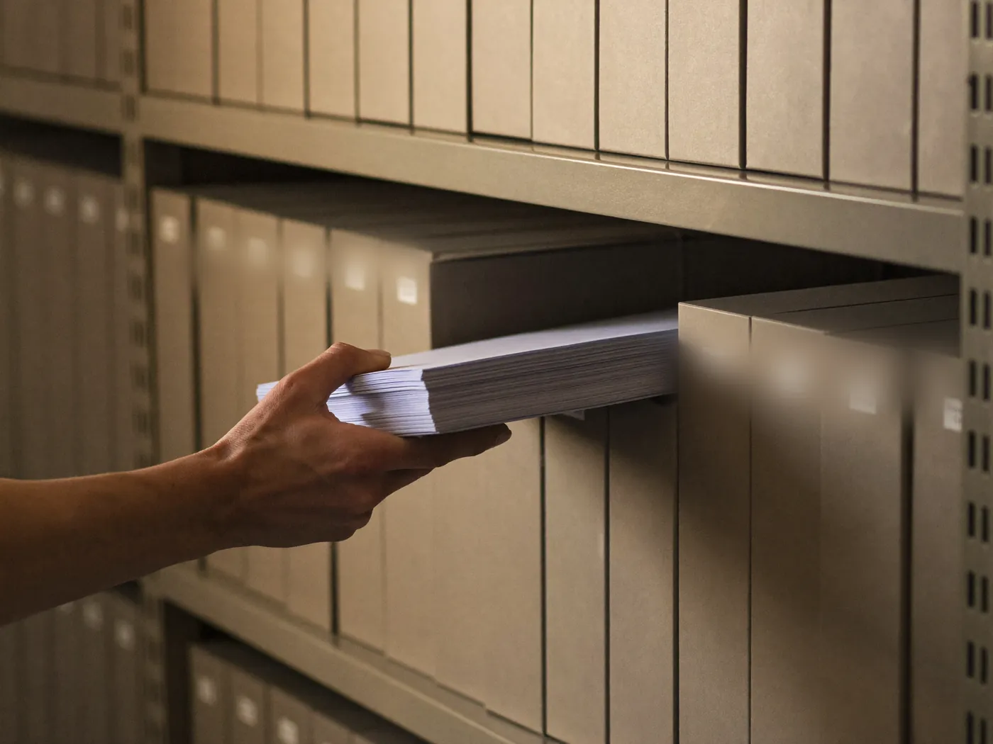 A hand filing papers into a wall of plain archive boxes