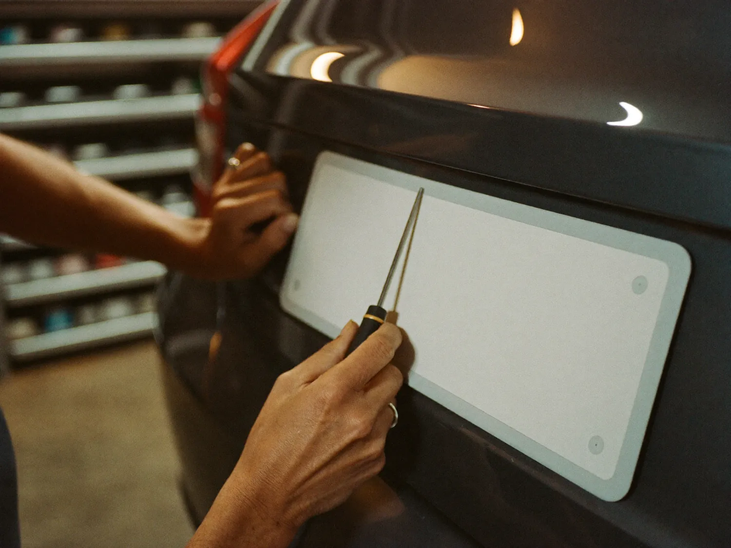 Hands fitting a blank number plate to the back of a car