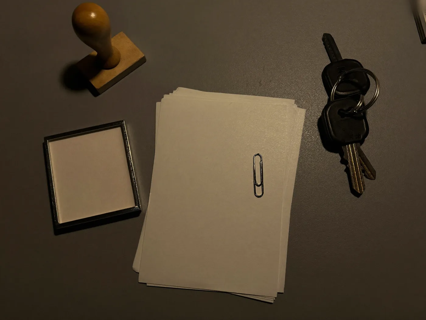 A rubber stamp, ink pad, blank papers and car keys on a desk