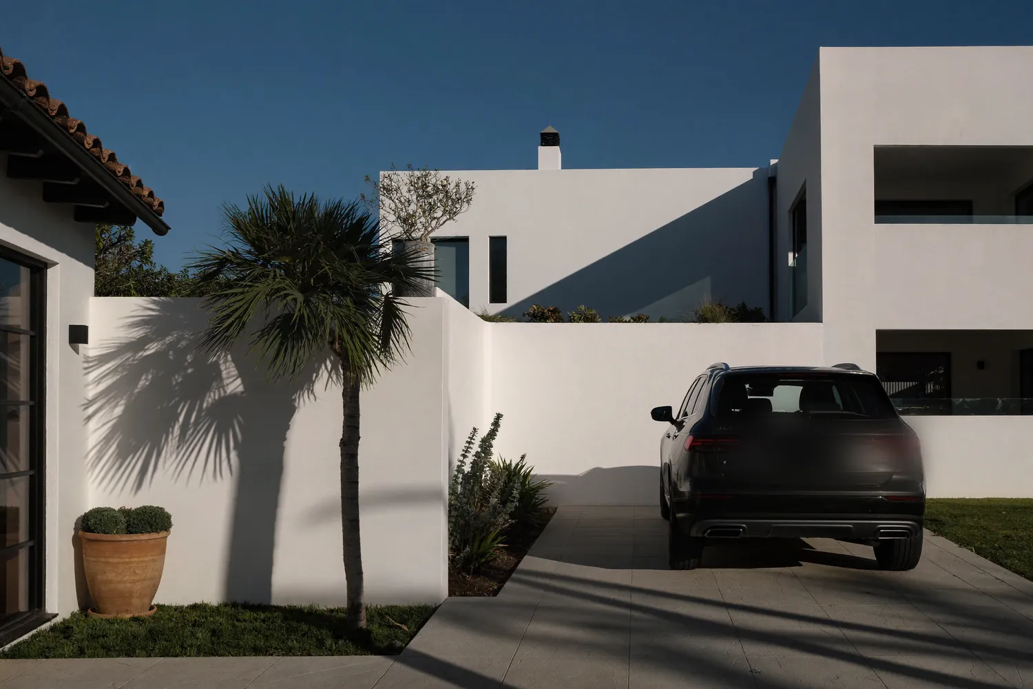 A car on a white villa driveway with palm shadows